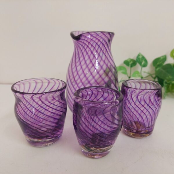 吹きガラスで作った酒器セットです。透明のがらすで作った徳利とぐい呑みに、緩くカーブして描かれた沢山の紫色の線が重なり合い、とても美しいです。