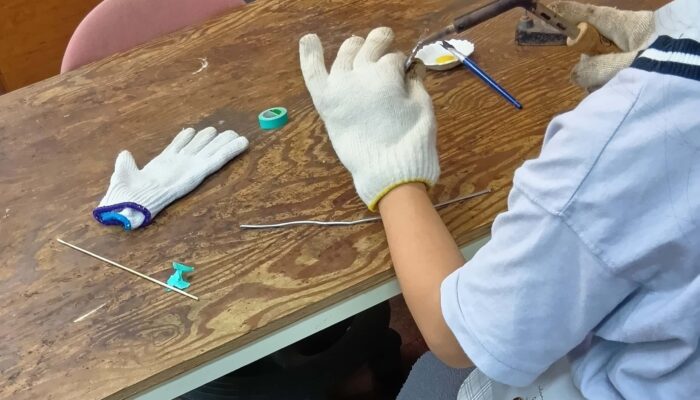 小学生がステンドグラス体験でハンダ付けをしています。
