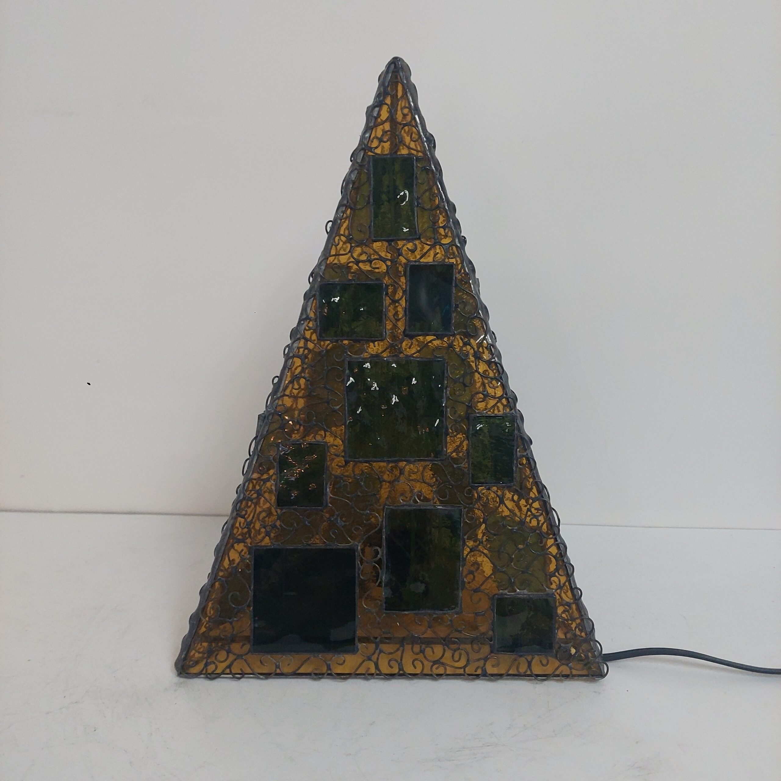 ステンドグラス、三角錐の置き型ランプです。秋の森をイメージし、黄色のガラスをベースに、緑のガラスにこの模様をサンドブラストしたガラスを重ねました。 細かくワイヤーを貼付け、蔓がランプをつたっているように見えます。
