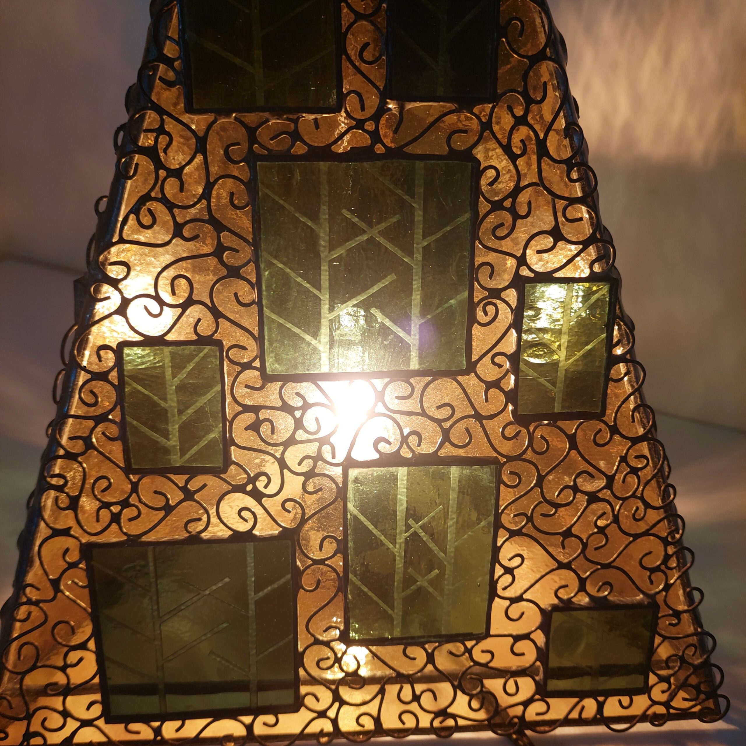 ステンドグラス、三角錐の置き型ランプです。秋の森をイメージし、黄色のガラスをベースに、緑のガラスにこの模様をサンドブラストしたガラスを重ねました。 細かくワイヤーを貼付け、蔓がランプをつたっているように見えます。