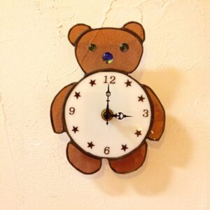 ステンドグラスのクマの時計です。白いお腹が文字盤になっているかわいい時計です。アナログの掛け時計です。目や鼻はナゲットでかわいらしい模様が入っています。アーティストショップＡ＆ＭＯ２のオリジナルデザインです。